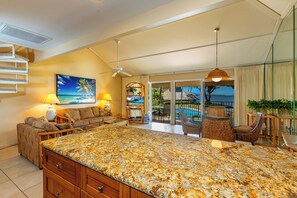 A spacious living area with a large kitchen island, a sofa, and a dining area with a view of the pool. - Ma'alaea Surf #G-7 – Coastal Comfort with Modern Amenities (Kihei)
