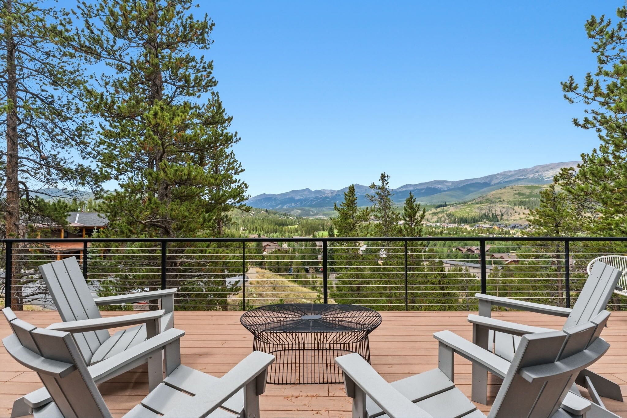 An outdoor deck with seating and a fire pit, overlooking a mountainous landscape.