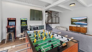 A room with a foosball table, a television, and a staircase. - Breck A-Frame Ski + Golf Retreat | Hot Tub + Sauna (Breckenridge)