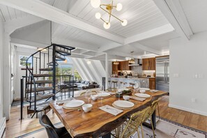 Un comedor amplio con una larga mesa de madera dispuesta para una comida, una escalera en espiral y vistas al exterior.