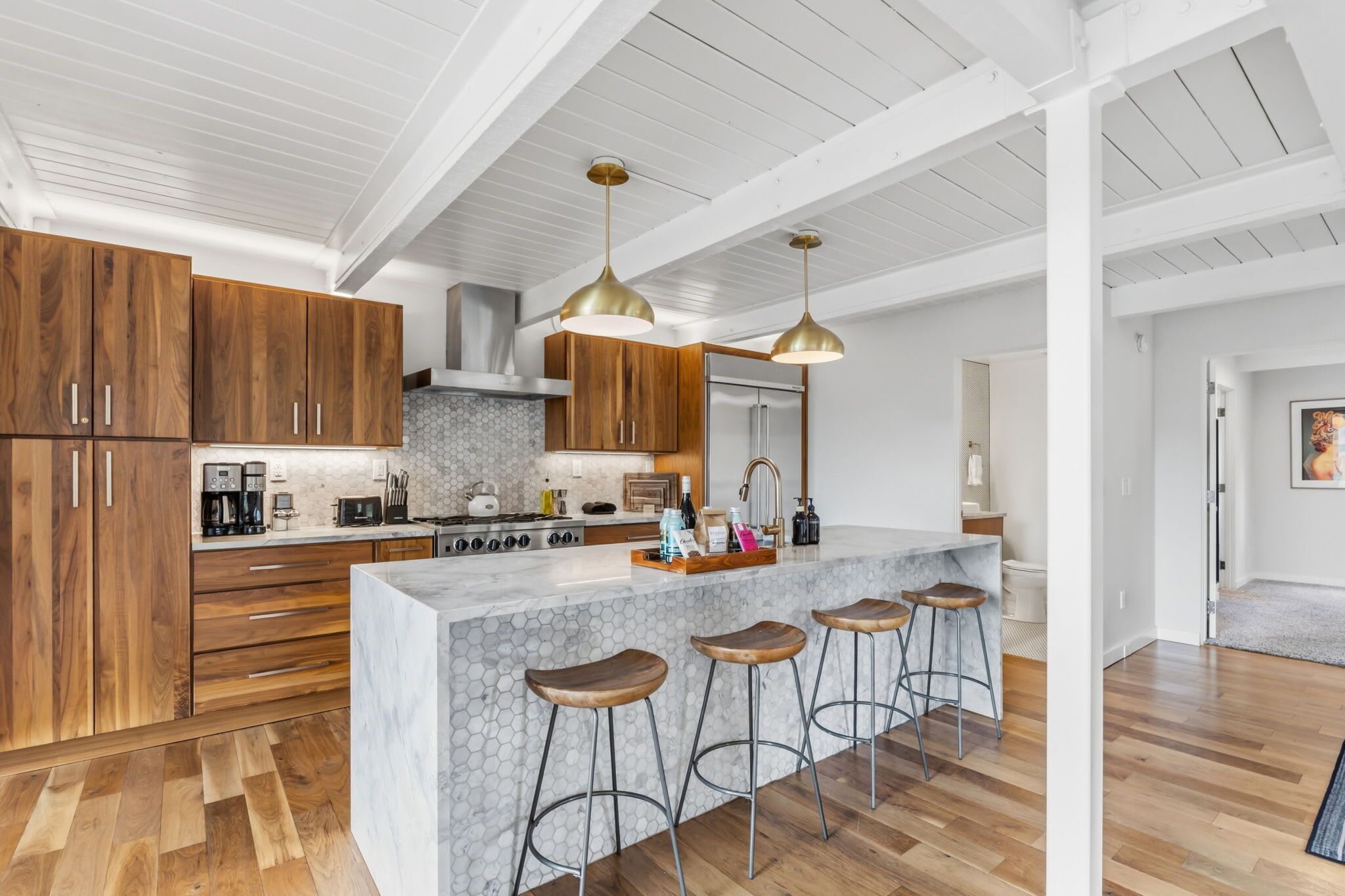 A modern kitchen with wooden cabinets, a marble island, bar stools, and pendant lighting.