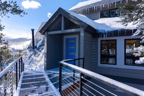 Un edificio moderno con una puerta azul, un balcón con barandas de metal y una montaña nevada al fondo.