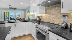 A modern kitchen with white cabinets, a granite countertop, a stove, a blender, and a view of the outdoors. - Conley  A Sound Front Townhome with Boat Slip! (Wrightsville Beach)