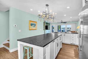 A kitchen with a central island, white cabinets, a chandelier, and a view through the window. - Conley A Sound Front Townhome with Boat Slip! (Wrightsville Beach)