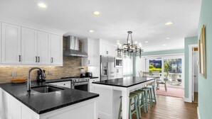 A modern kitchen with white cabinets, a black countertop, and a central island with bar stools. - Conley  A Sound Front Townhome with Boat Slip! (Wrightsville Beach)
