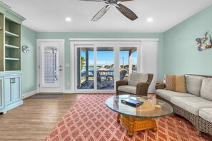 A living room with a glass coffee table, wicker furniture, a ceiling fan, and a view through glass doors. - Conley A Sound Front Townhome with Boat Slip! (Wrightsville Beach)