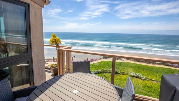 A balcony with a view of the ocean, a round table, and outdoor seating.