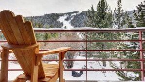 A wooden Adirondack chair on a balcony overlooking a snowy mountain landscape with a ski slope. - Keystone Summer Stay | Balcony & River Views (Keystone)