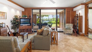 A spacious living room with a sofa, television, and a view of the outdoors. - 1st Floor Mauna Lani Terrace Condo - Private Beach Access! (Kamuela)