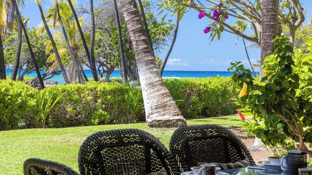A table set for dining with chairs, a view of the ocean, and palm trees. - 1st Floor Mauna Lani Terrace Condo - Private Beach Access! (Kamuela)