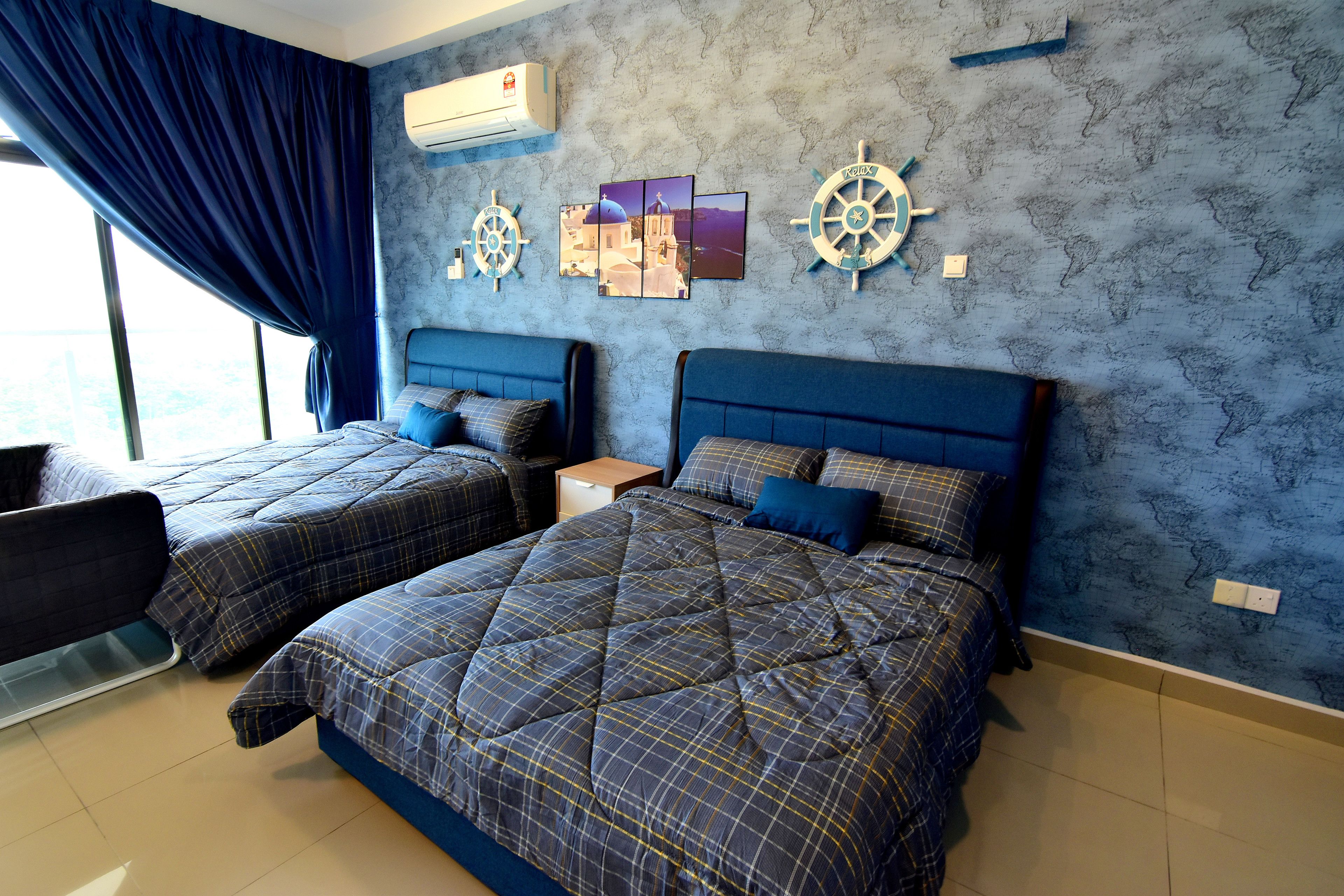 A hotel room with two beds, a large window with blue curtains, and nautical-themed wall decor.