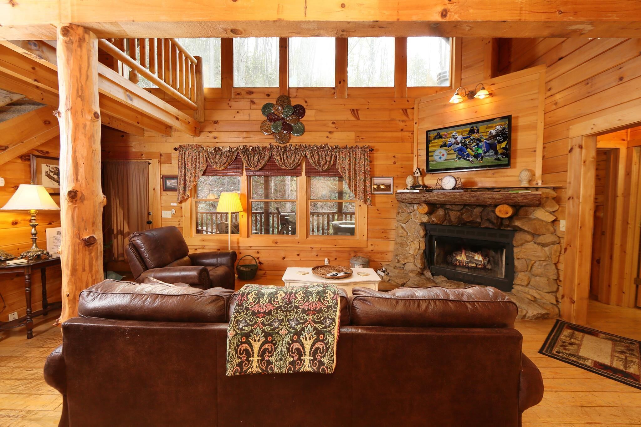 A cozy log cabin interior with a fireplace, leather sofa, and a dining table.