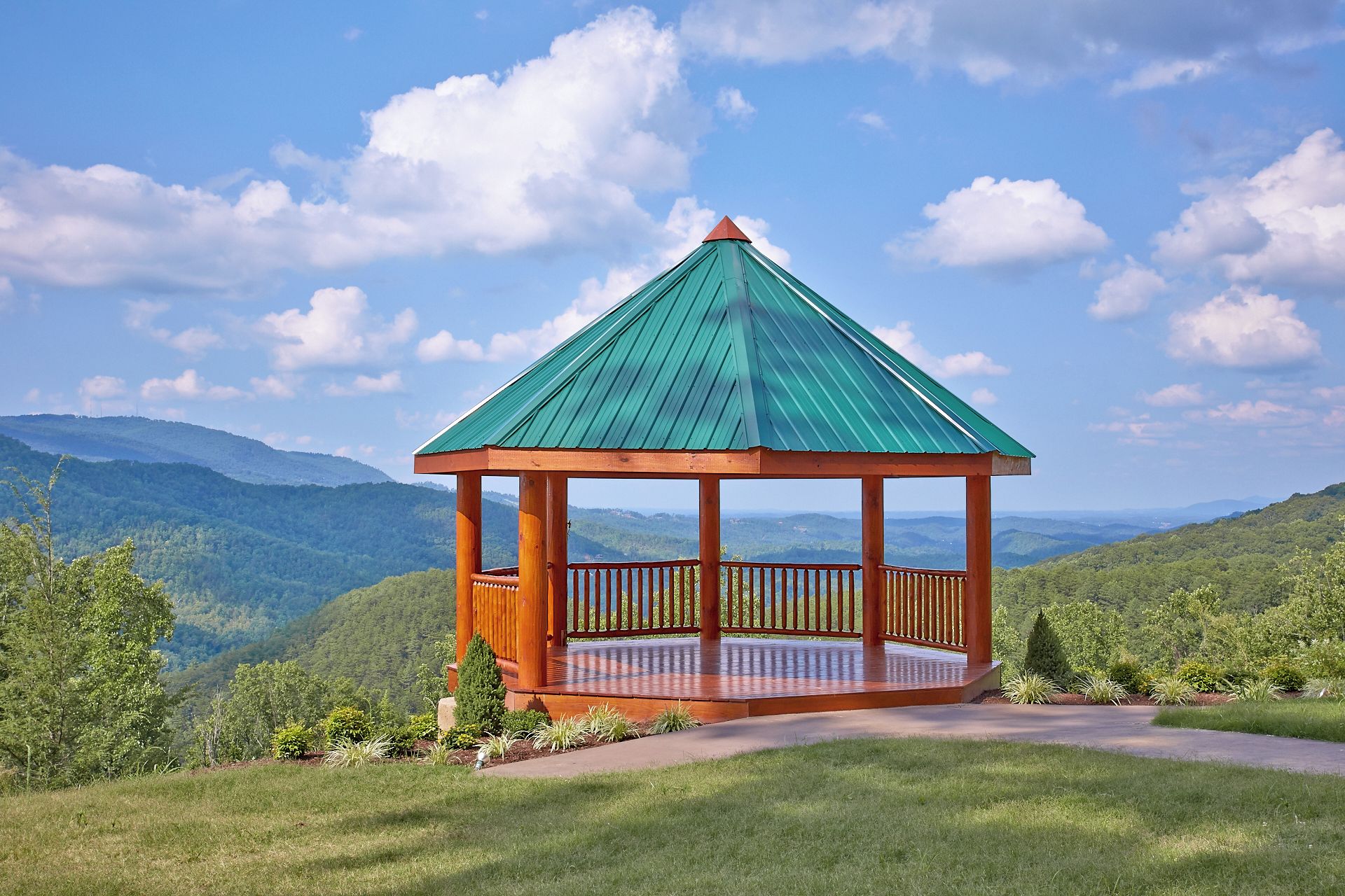 Un mirador de madera con techo verde, rodeado de abundante vegetación y un paisaje montañoso.