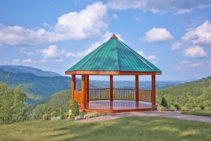 A wooden gazebo with a green roof, surrounded by lush greenery and a mountainous landscape. - Wood Burning Fireplace | Secluded | Hot Tub | Wifi | Fireplace (SEVIERVILLE)