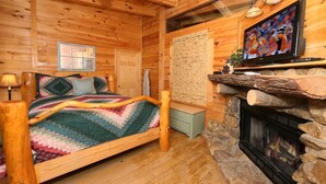 Een knus houten blokhutkamer met een bed, een stenen open haard en een televisie erboven.