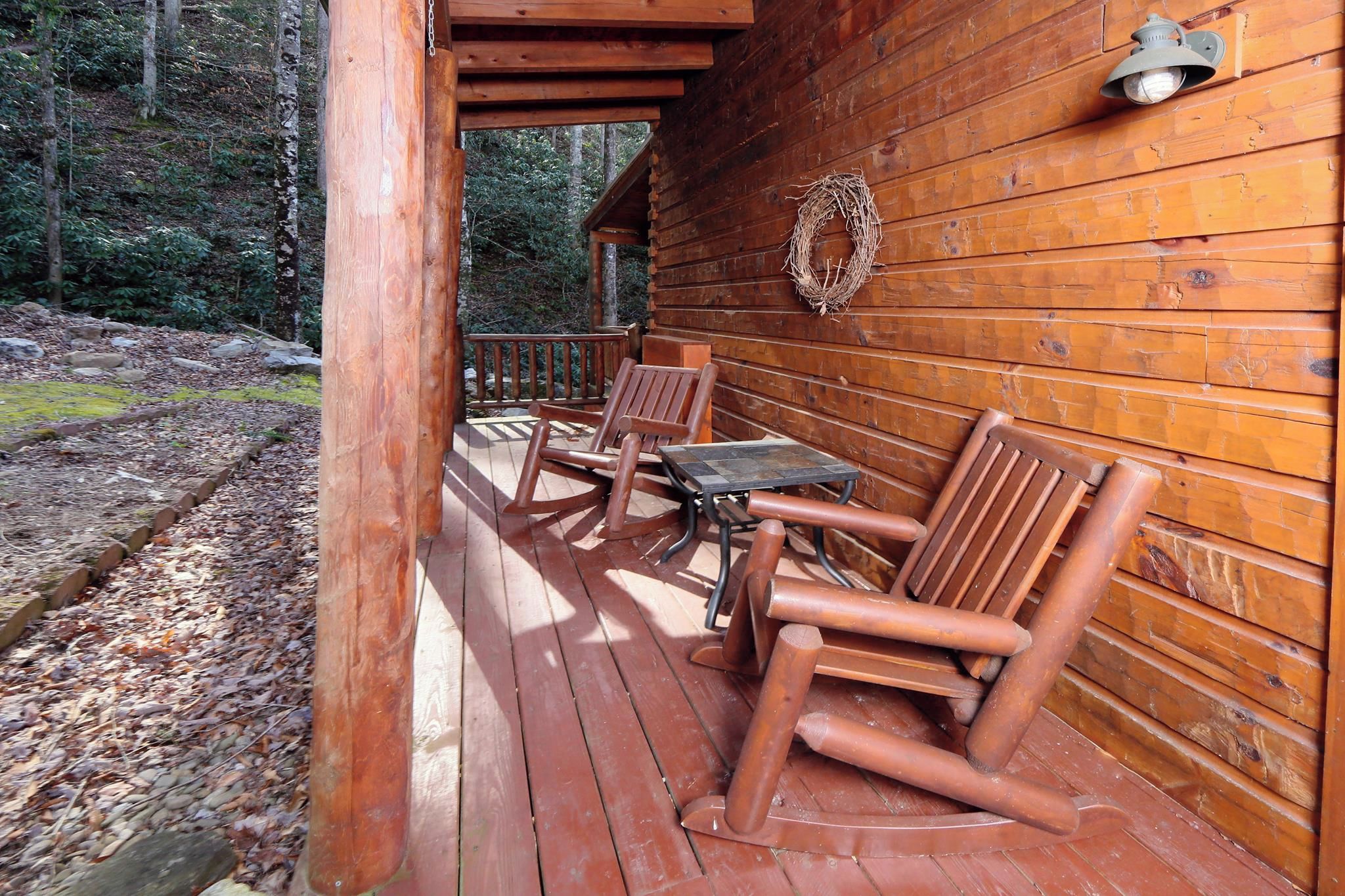A wooden cabin with a porch featuring two wooden chairs and a table.