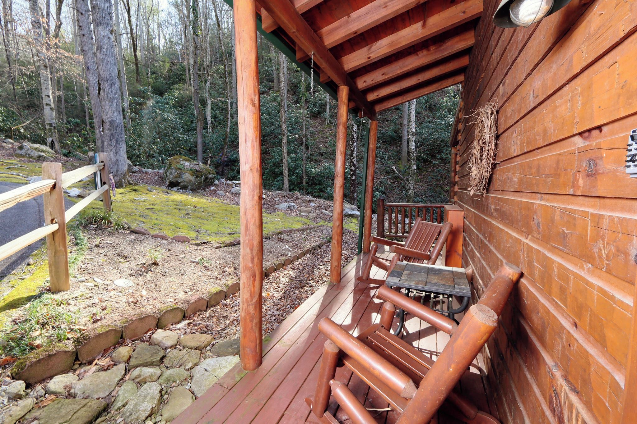 Eine Holzterrasse mit Tisch und Stühlen, umgeben von einer Steinsicht und einem Wald im Hintergrund.