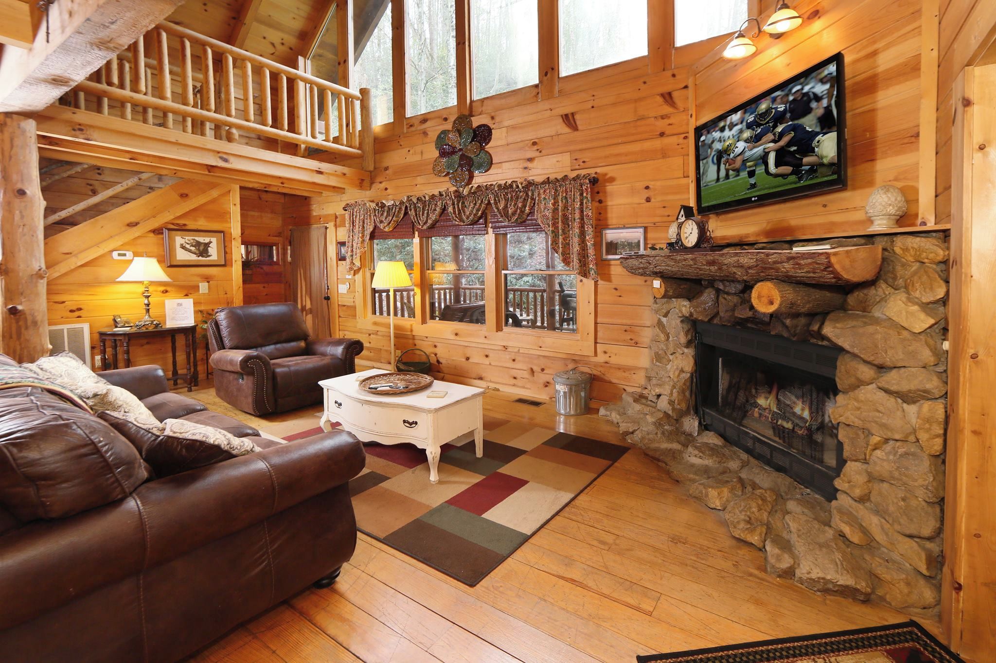 Accogliente interno di una baita in legno con camino, divani in pelle, televisione e un balcone con ringhiera.