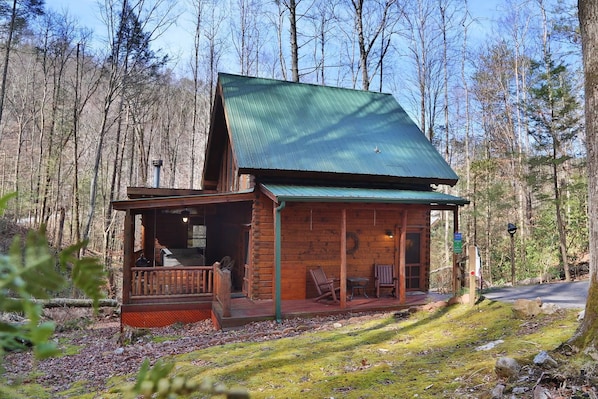 A rustic cabin with a porch and seating area, surrounded by a forest.