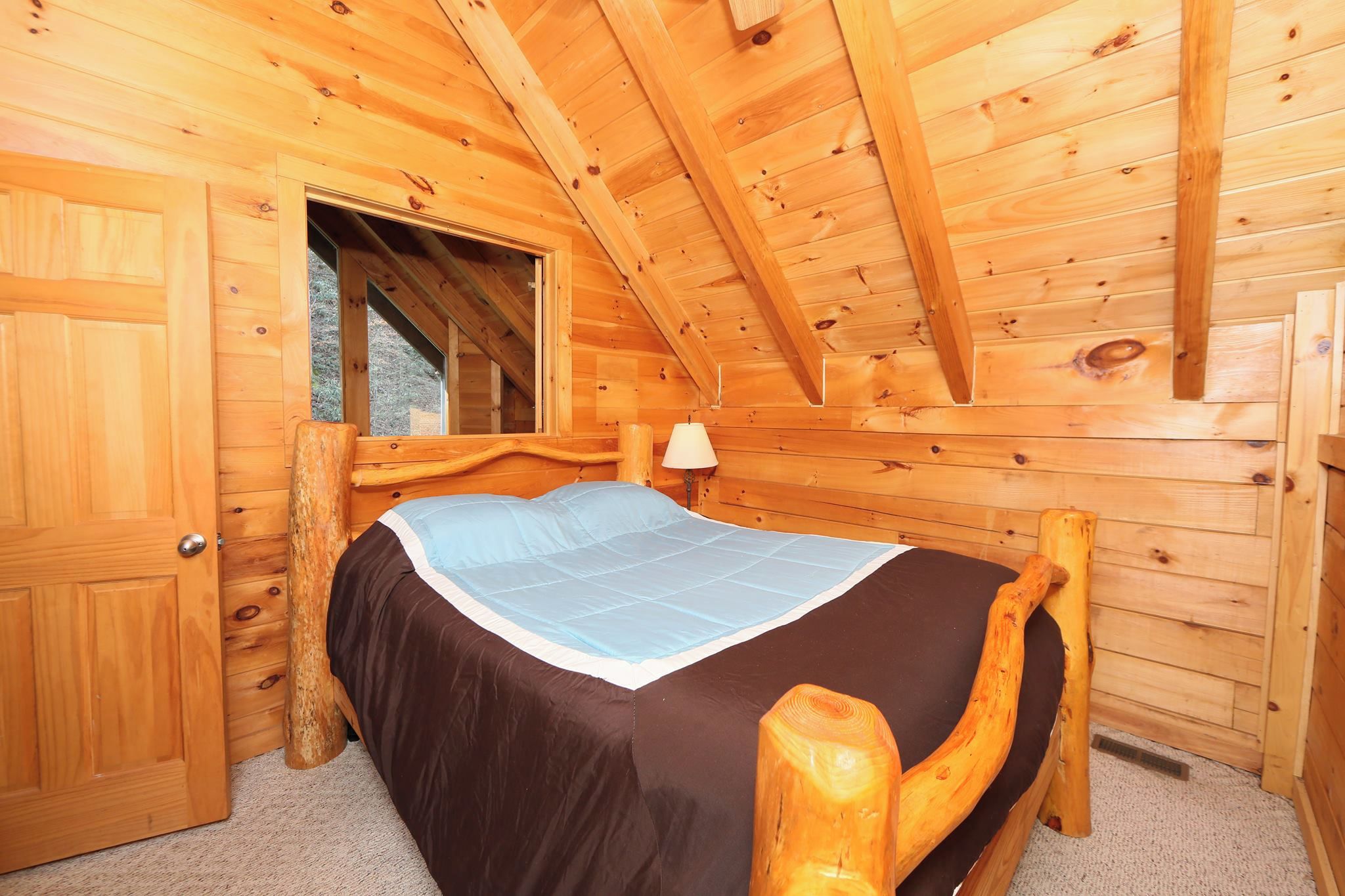 Une chambre dans une cabane en bois, avec un lit, une fenêtre et une porte.