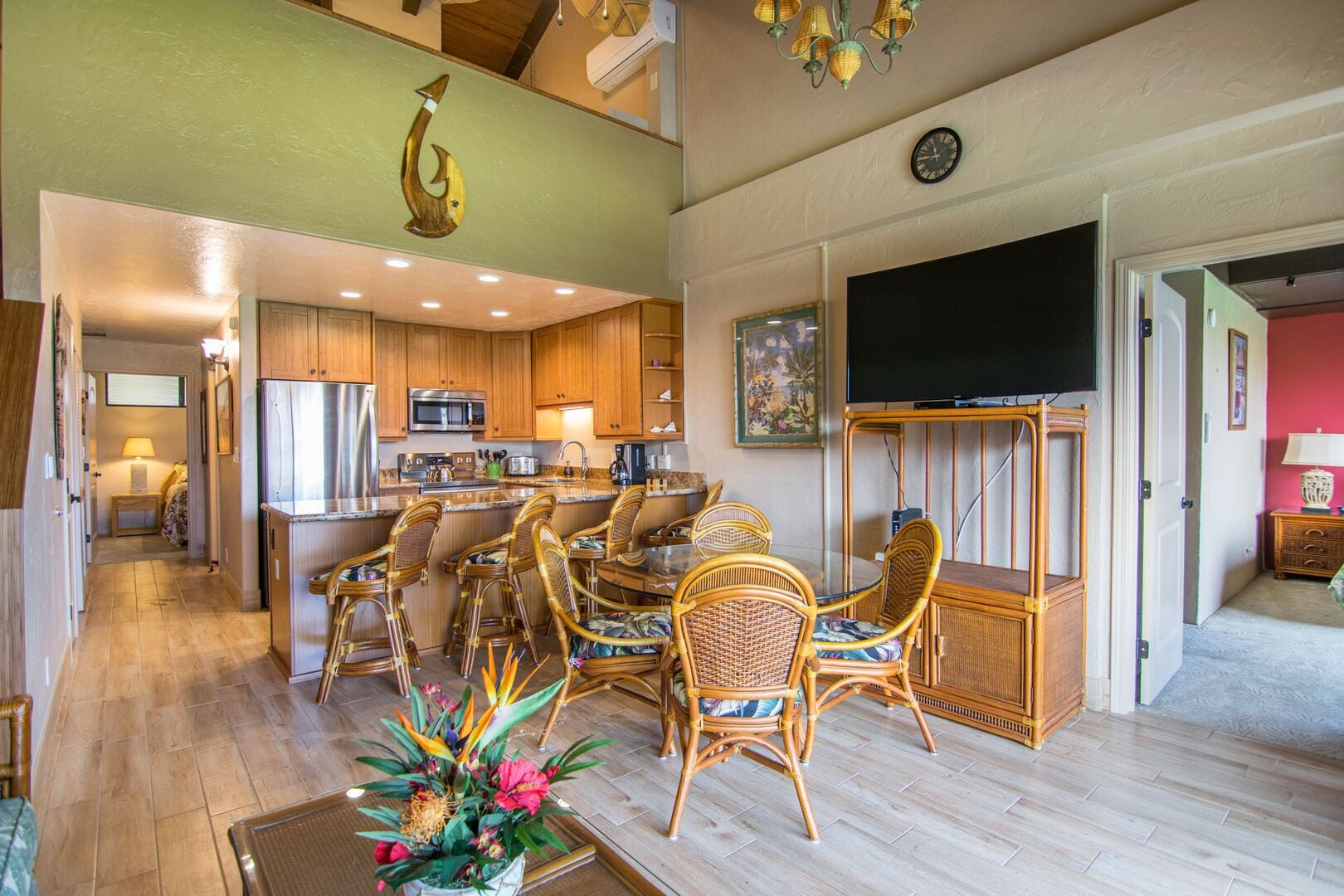 A spacious living area with a dining set, kitchen, and a flat-screen TV mounted on the wall.
