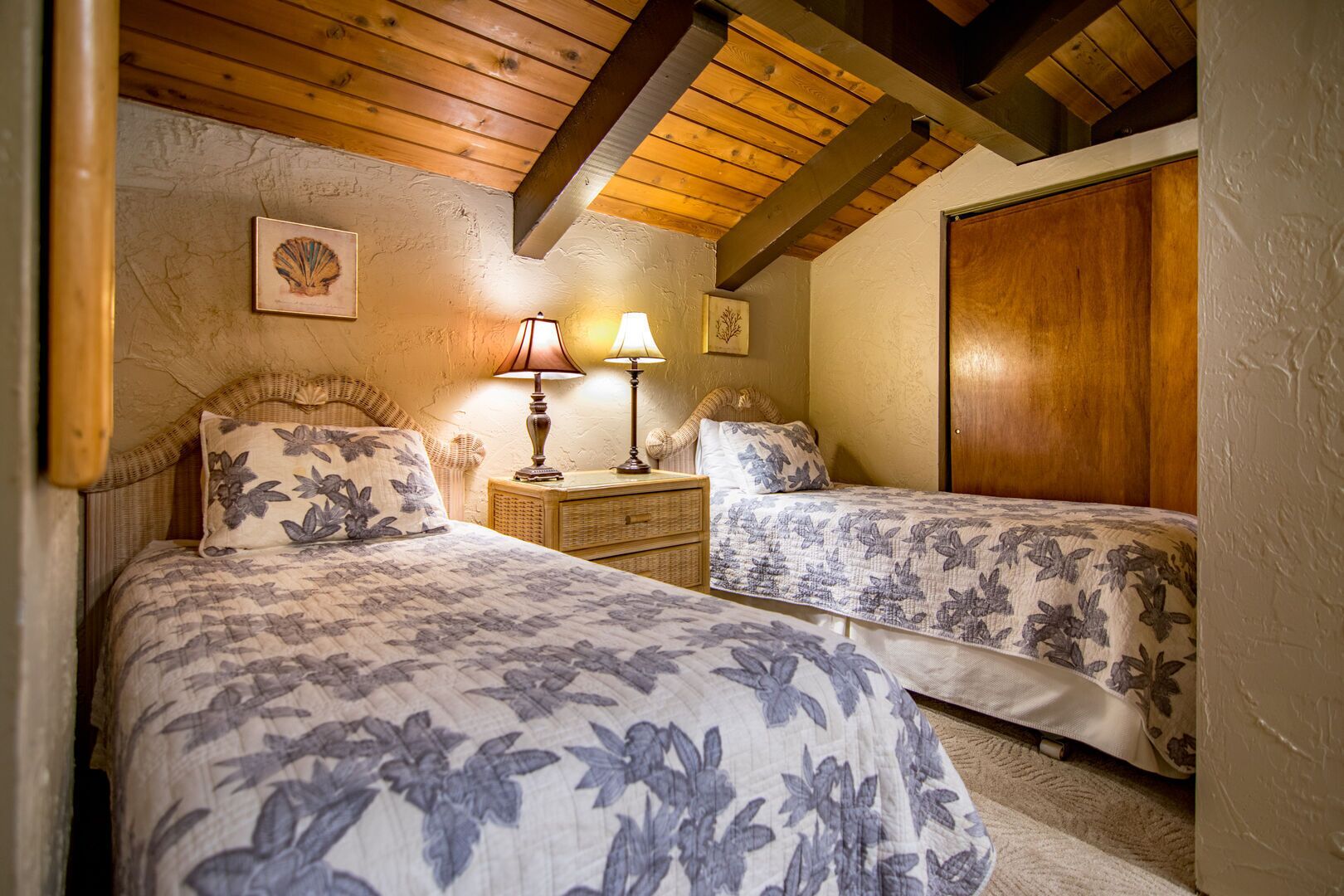 Un dormitorio con dos camas, cabeceros de madera, una mesita de noche con lámparas y un armario de madera.