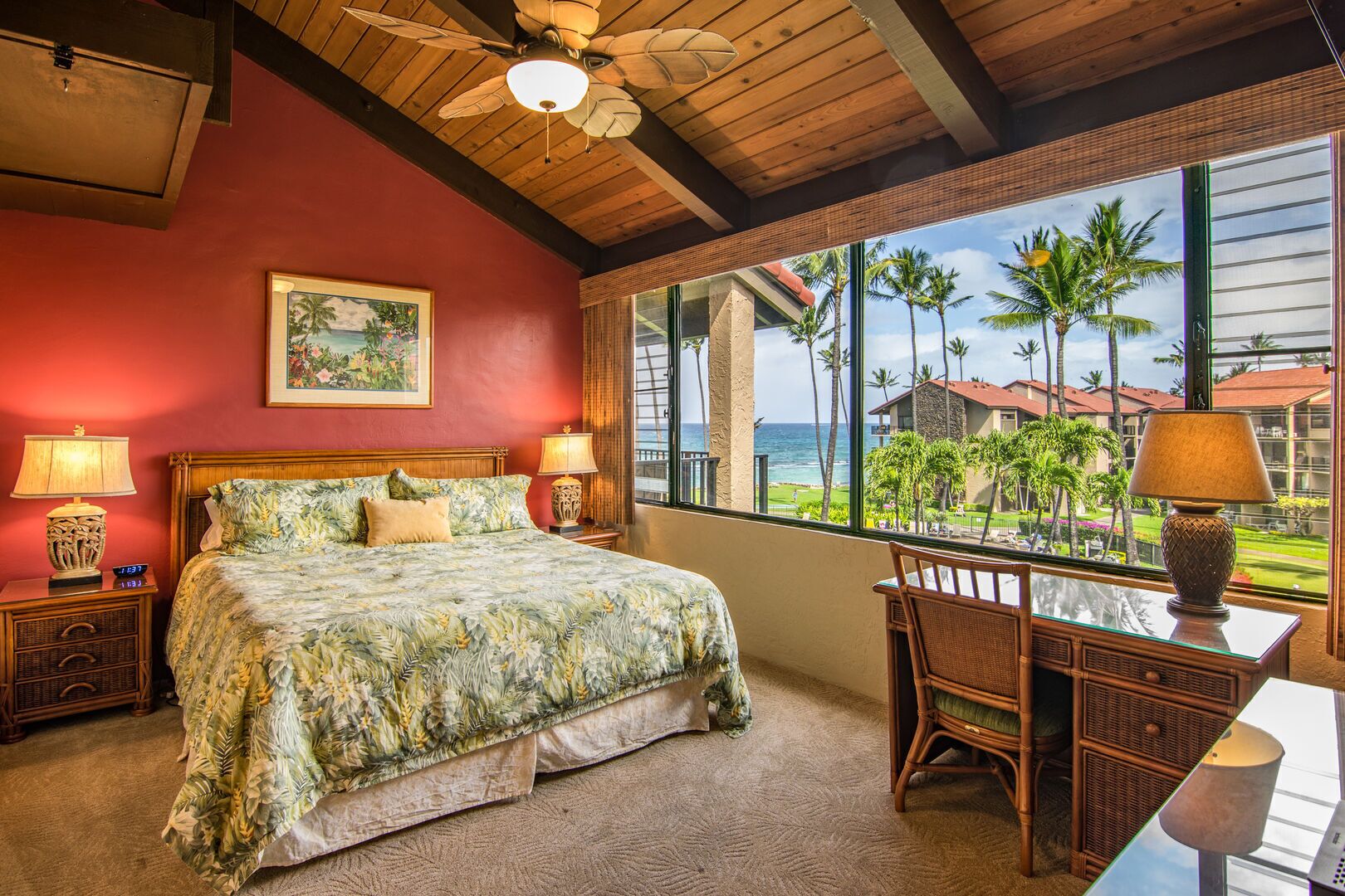 Une chambre à coucher comprenant un lit, deux tables de chevet, une chaise, un bureau et une grande fenêtre donnant sur des palmiers et un immeuble.