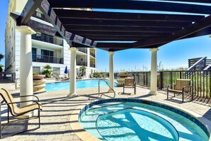 A rooftop pool area with lounge chairs, a covered seating area, and a building with balconies.