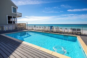 A swimming pool with a view of the ocean, deck chairs, and a poolside area.