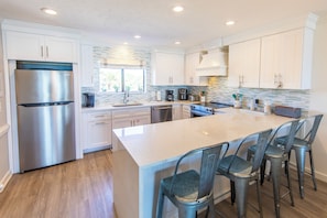 A modern kitchen with white cabinetry, stainless steel appliances, and a large island with bar stools.