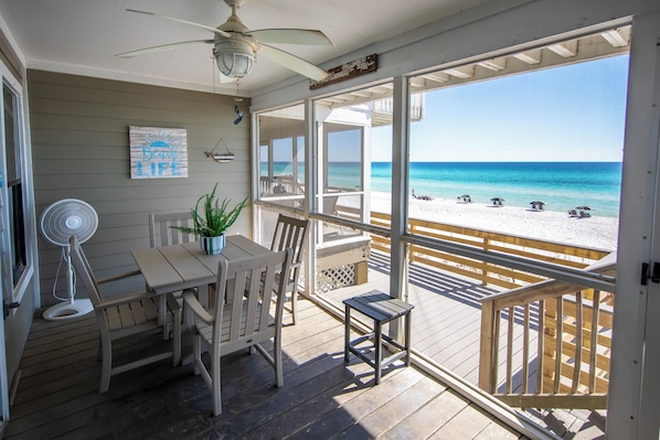 A beachside room with a view of the ocean, a ceiling fan, a table with chairs, and a small table with a plant.