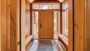 A wooden hallway with a central door, benches on either side, and a patterned rug on the floor.