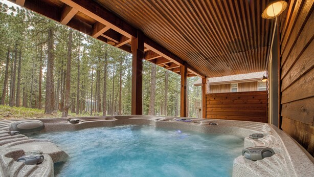 A hot tub with a view of a forest, wooden beams, and a wooden wall.
