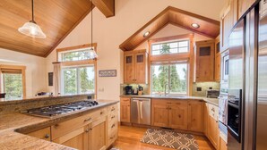 A kitchen with wooden cabinets, granite countertops, stainless steel appliances, and large windows offering a view of the outdoors.