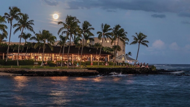 A beachfront hotel with a large building, palm trees, and a view of the ocean. - Lawai Beach 1401 Oceanfront By Suite Paradise (Koloa)