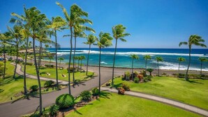 A coastal view with palm trees, a road, and ocean waves. - Lawai Beach 1401 Oceanfront By Suite Paradise (Koloa)