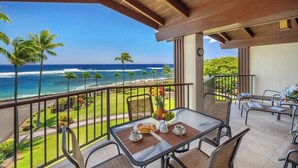 A balcony with a table set for breakfast, overlooking a beach with palm trees and the ocean. - Lawai Beach 1401 Oceanfront By Suite Paradise (Koloa)