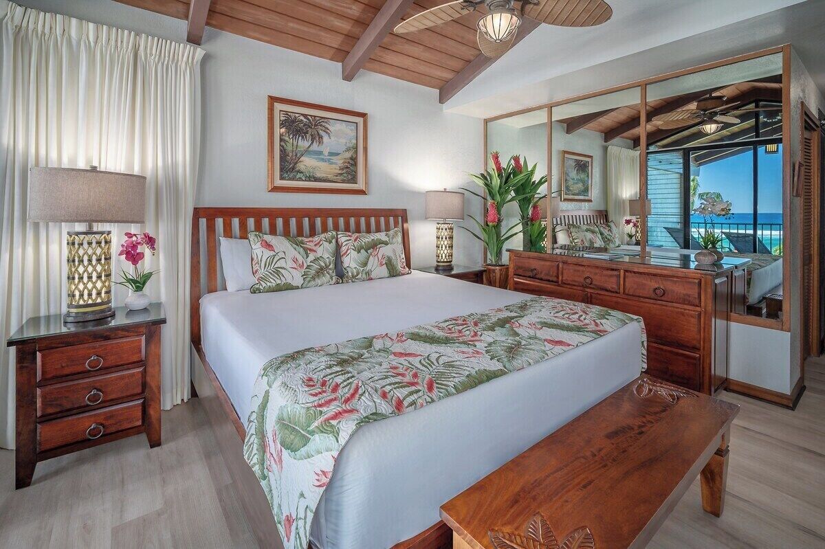 Een ruime slaapkamer met een groot bed, houten hoofdbord en uitzicht op de oceaan door een schuifdeur.
