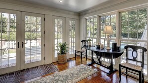 A room with a dining table, chairs, a lamp, and large windows with a view of greenery. - Premium DOG FRIENDLY 4th Row Ocean Sea Pines Home with a Private Pool & Spa (Hilton Head Island)