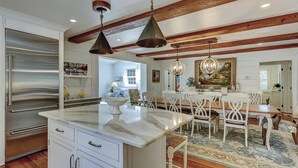 A kitchen with a large island, stainless steel appliances, and a dining area with white chairs and a chandelier. - Premium DOG FRIENDLY 4th Row Ocean Sea Pines Home with a Private Pool & Spa (Hilton Head Island)
