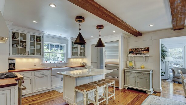 A kitchen with white cabinets, a wooden island with stools, pendant lighting, and a built-in oven. - Premium DOG FRIENDLY 4th Row Ocean Sea Pines Home with a Private Pool & Spa (Hilton Head Island)