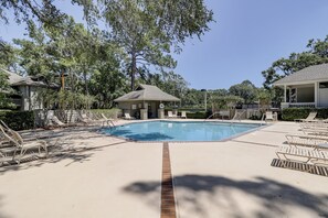 Una piscina con sillas de descanso y un pequeño edificio, rodeado de árboles y un cielo despejado.