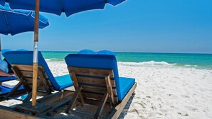 A beach scene with two wooden lounge chairs under blue umbrellas, facing the ocean. - BEACHFRONT CONDO! 8TH FLOOR! FREE BEACH SERVICE (Panama City Beach)