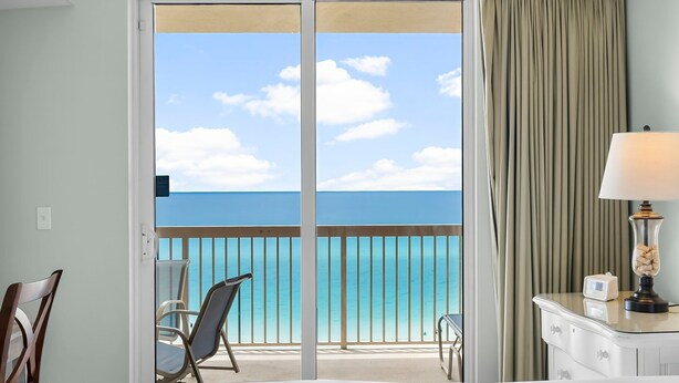 A hotel room with a balcony, a bed, a chair, a lamp, and a view of the ocean. - BEACHFRONT CONDO! 8TH FLOOR! FREE BEACH SERVICE (Panama City Beach)