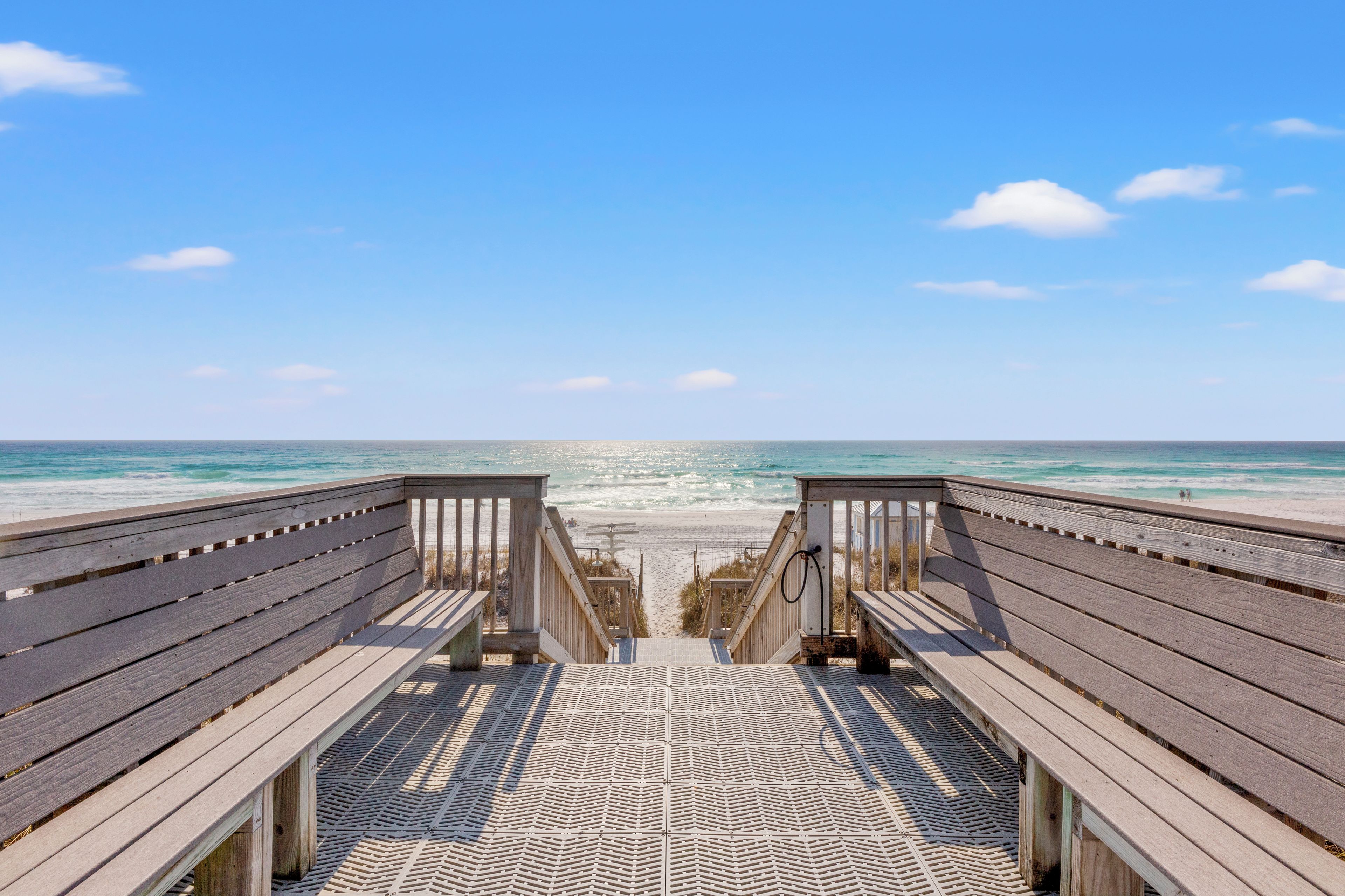 A wooden boardwalk leading to a beach with a clear view of the ocean.