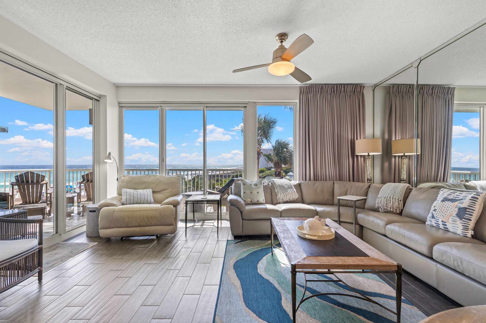 A spacious living room with a large window overlooking the ocean, furnished with a sofa, armchairs, and a coffee table.