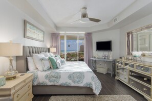 A bedroom with a large bed, a ceiling fan, a television, and a dresser.