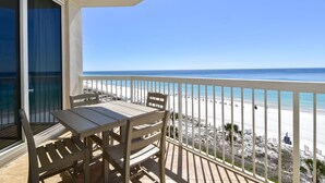 A balcony with a table and chairs, overlooking a beach with people and a clear sky. - Open Concept Beachfront Condo w/ Easy Beach Access in Central Destin! 🌴💙🌅 (Destin)