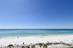 A beach with a clear sky, a sandy shore, and a few people walking.