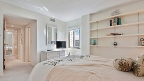 Un dormitorio con una cama, un tocador, un televisor y una estantería.